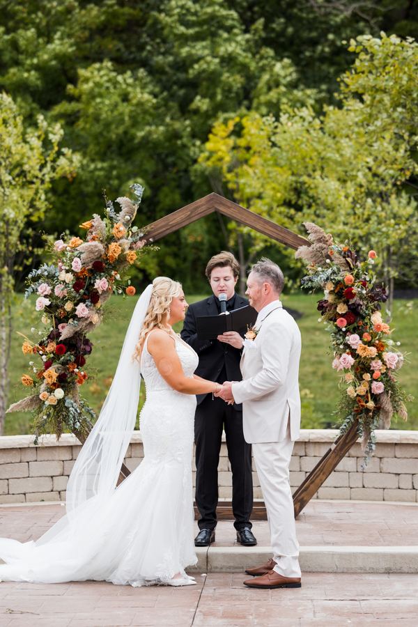 Reed officiating under a wooden arch dressed in autumn flowers